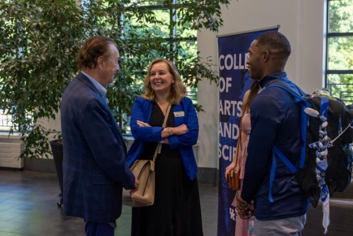 Man and woman in blue jackets talking with a student.