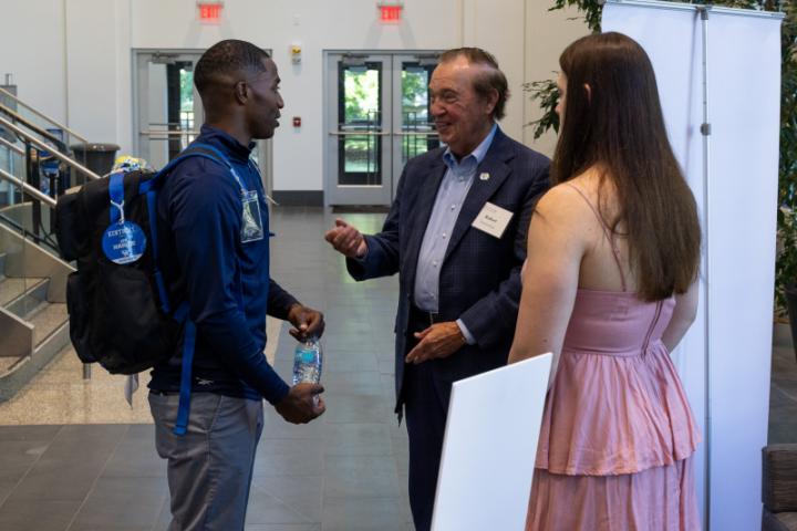 Older man speaking with two students in lobby.