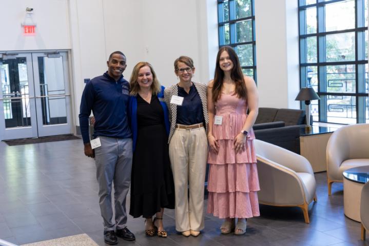 Four people posing together in bright lobby space.