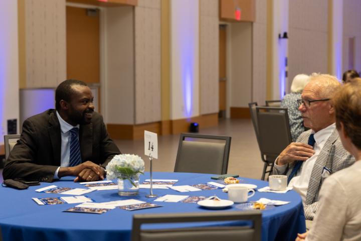 Three people chatting at round event table with blue tablecloth.