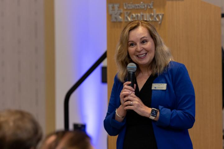 Woman in blue jacket speaking with microphone.