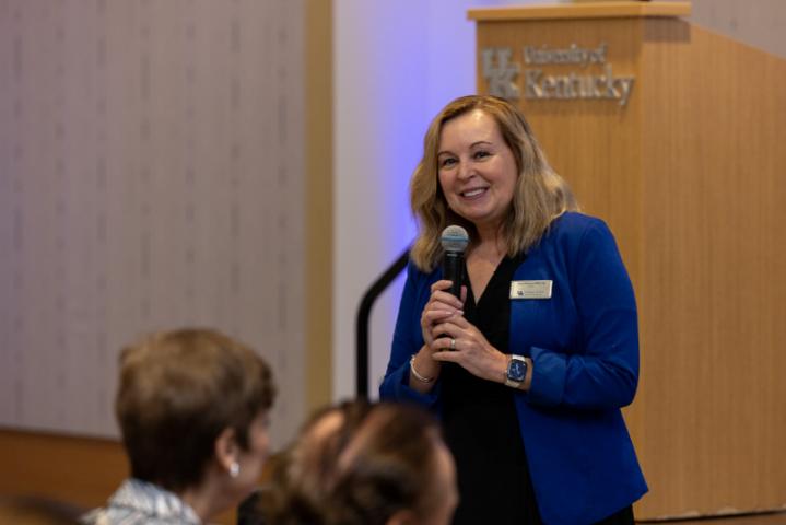 Woman in blue jacket speaking with microphone.