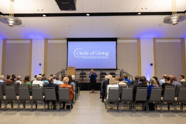 Wide view of speaker on stage with "Circle of Giving" screen.
