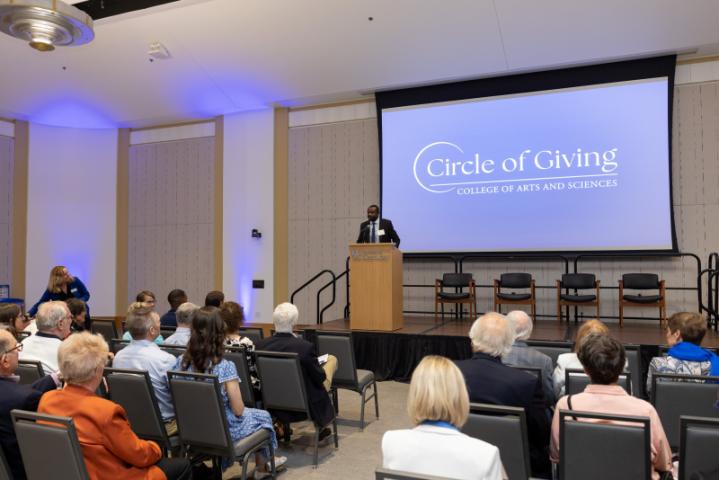Man at podium speaking under "Circle of Giving" screen.