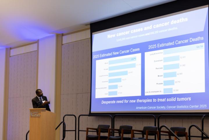 Presenter pointing to cancer data chart on large screen.