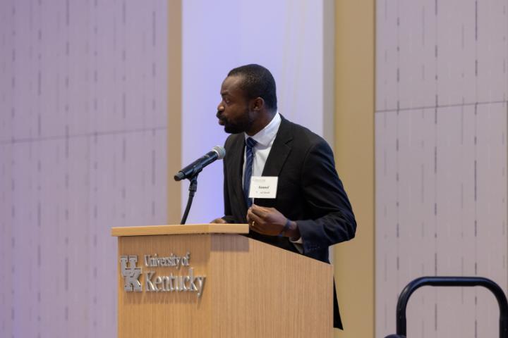 Man in suit speaking at podium with UK logo.