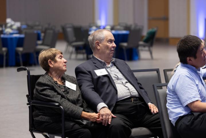 Couple holding hands while seated at event.