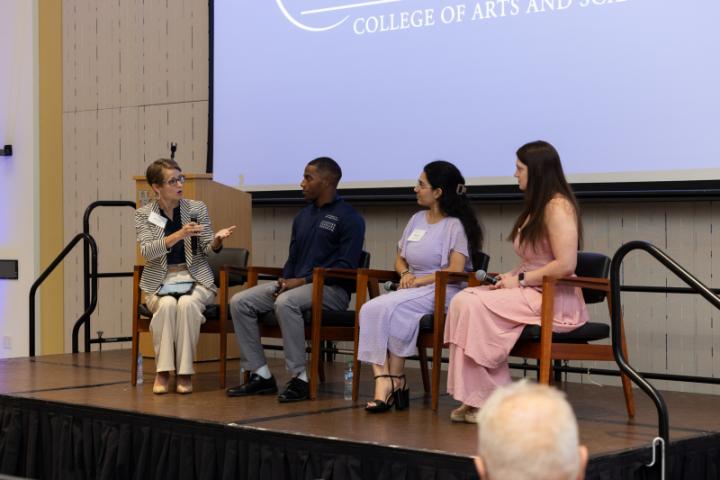 Panel of four people on stage, one speaking with hand gestures.