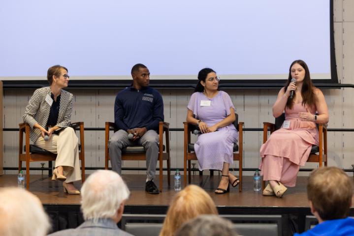 Panel discussion with woman in pink dress speaking into microphone.
