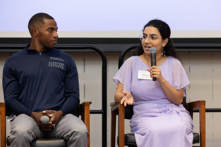 Woman in lavender dress speaking into microphone during panel.