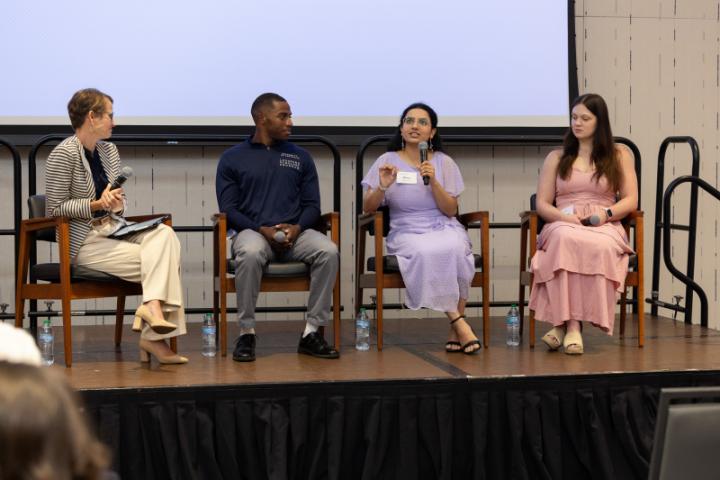 Panelist in lavender dress speaking while others listen.