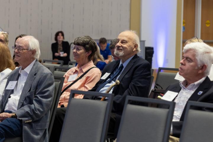 Audience members seated, some smiling while listening.