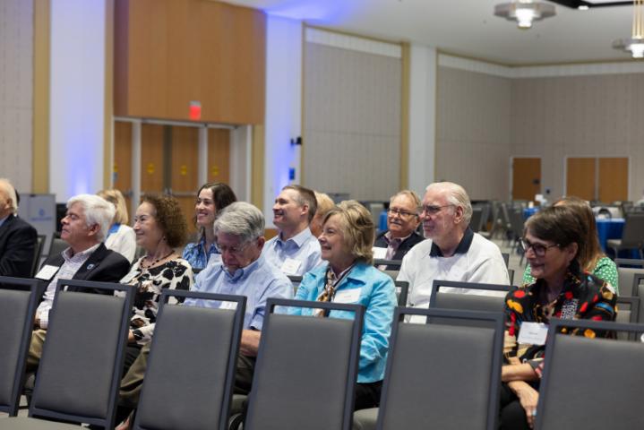 Audience members smiling and engaged while listening.