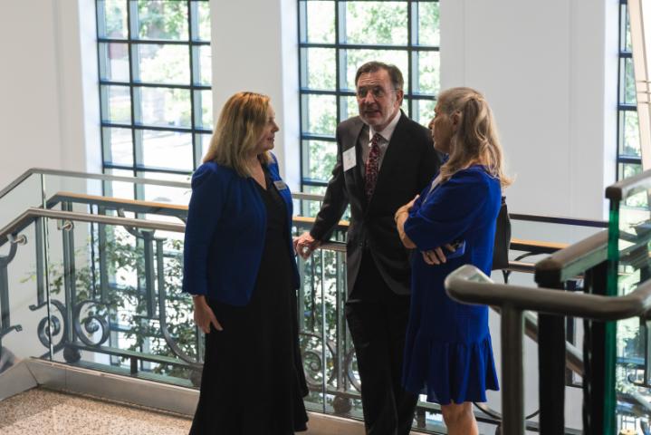 Three people in blue outfits and suit conversing by staircase.