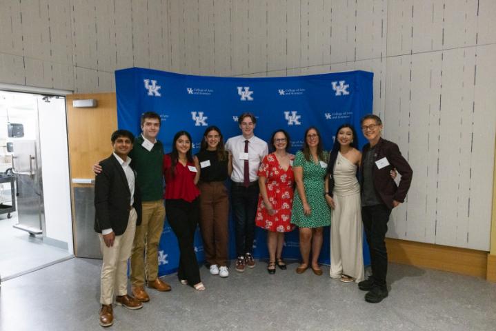 Large group posing in front of UK College of Arts and Sciences backdrop.