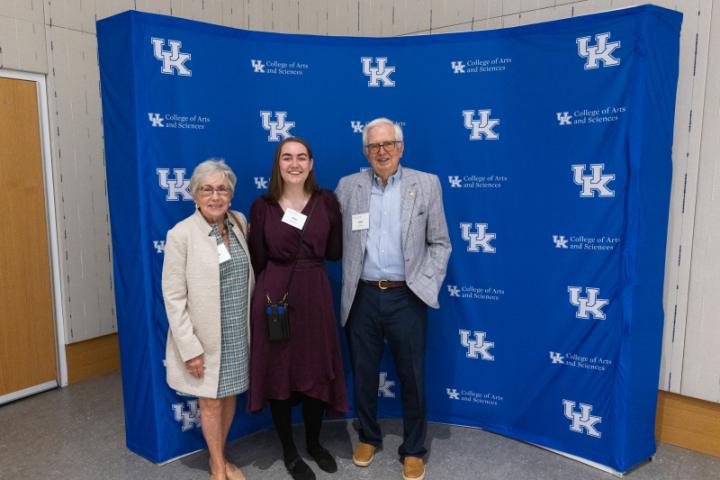 Three people posing together in front of UK A&S backdrop.
