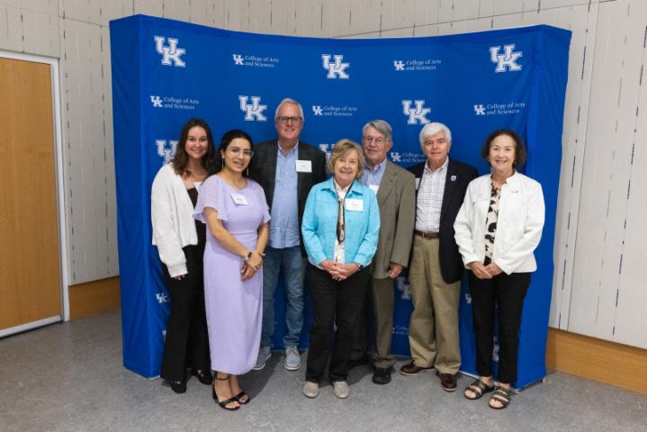 Group of seven smiling in front of UK A&S backdrop.