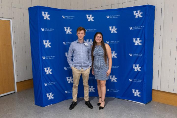 Two students posing together in front of UK A&S backdrop.