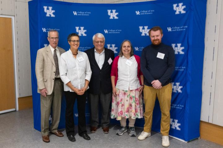 Group of five smiling in front of UK A&S backdrop.