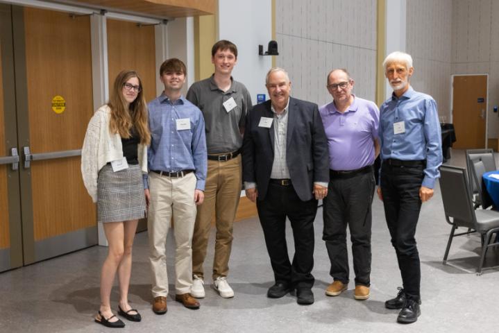 Six people posing together in event space with round tables.