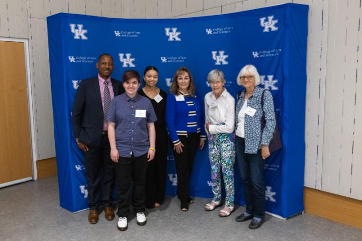 Group of six smiling in front of UK A&S backdrop.