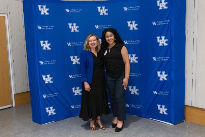 Two women posing side by side in front of UK A&S backdrop.