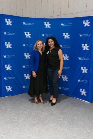 Two women smiling together in front of UK A&S backdrop.