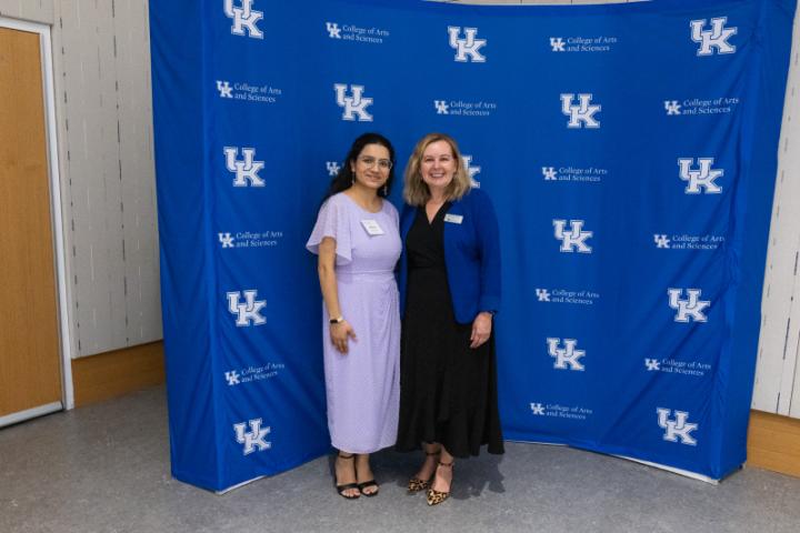 Two women in professional attire posing in front of UK A&S backdrop.