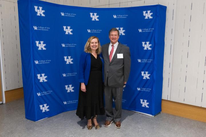 Woman in black dress and man in suit posing in front of UK A&S backdrop.