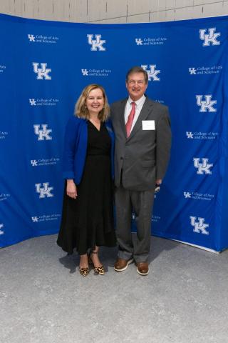 Woman in black dress and man in suit smiling together in front of backdrop.