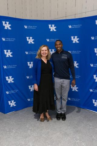 Woman in black dress and man in Lunsford Scholars shirt posing in front of UK A&S backdrop.