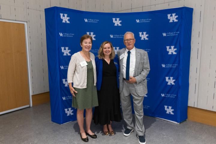 Three people posing together in front of UK A&S backdrop.