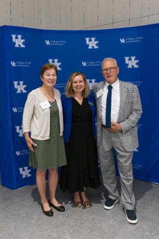 Three people smiling and posing together in front of UK College of Arts and Sciences backdrop.