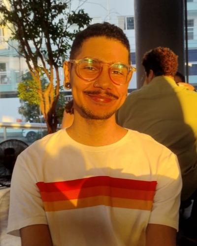 A man with short hair and glasses smiles while wearing a white t-shirt with red and orange stripes.