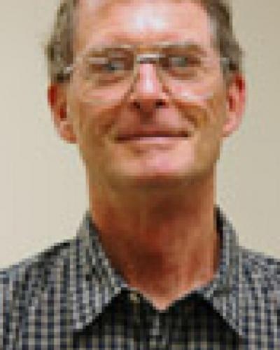 A man wearing glasses and a blue and white checkered collared shirt smiles at the camera.