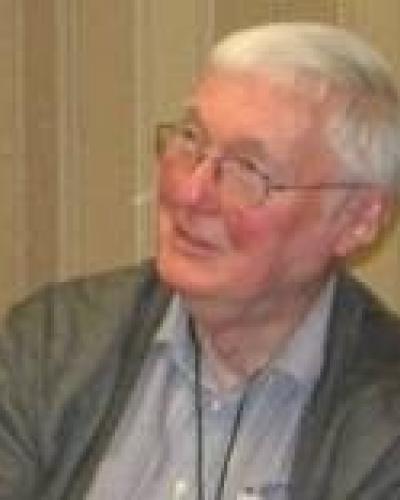 A man with white hair and glasses smiles as he looks to the left.