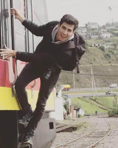 A man in black clothing and a backpack climbs onto a red and yellow train.