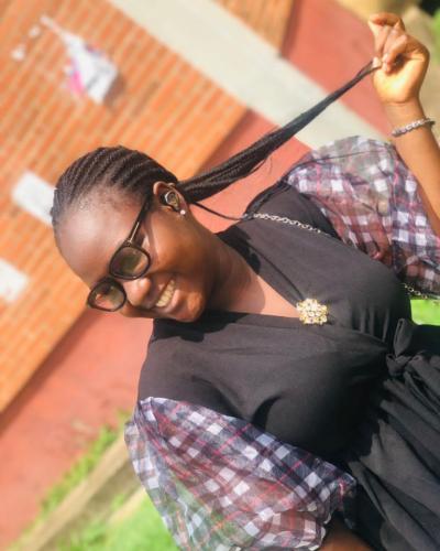 A woman with braided hair and glasses smiles while holding a strand of her hair.