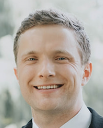 A smiling man in a suit and white shirt, facing the camera.