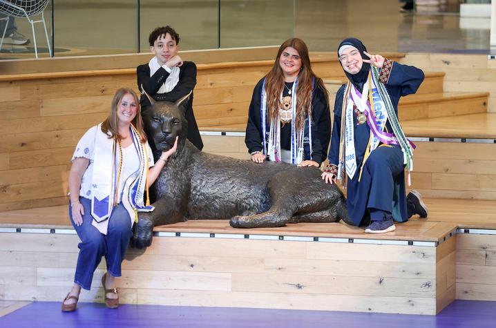four students it around a statue of a wildcat