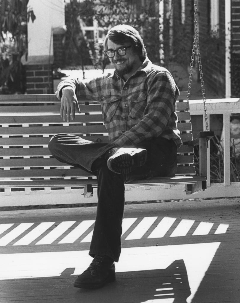 Gurney Norman sitting on a bench smiling