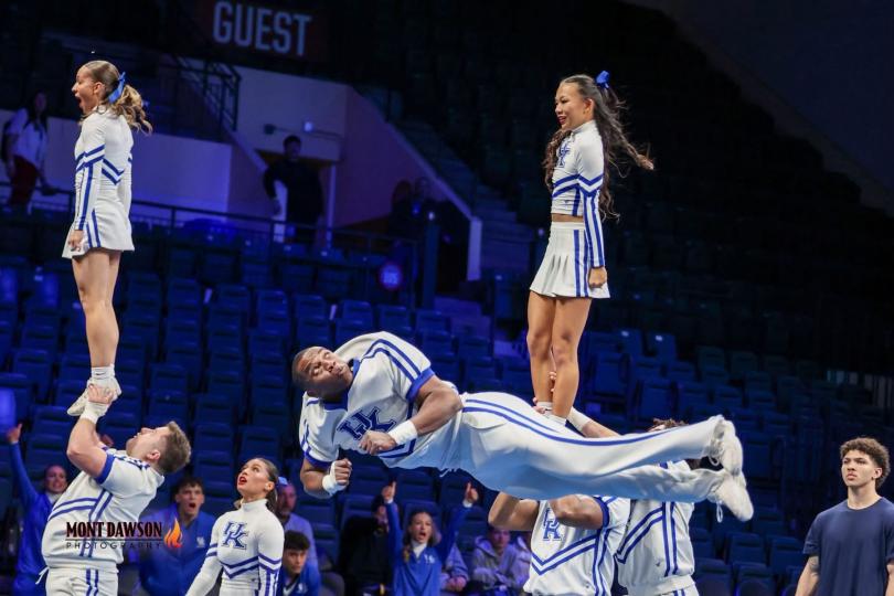 A male cheerleader is in the air horizontally. 